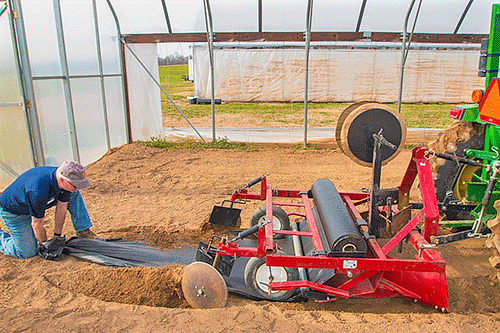 Laying plastic in a high tunnel in North Carolina. Extension at North Carolina A&T offers a plasticulture rental program that allows small farmers to try plasticulture without buying expensive equipment.
