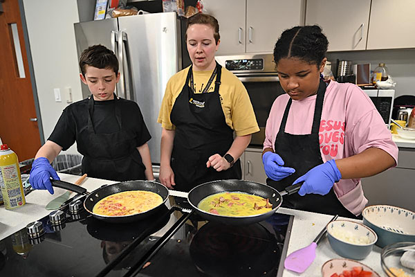 Instructor teaches students how to cook a meal in the kitchen.