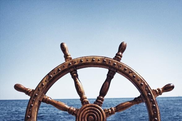 Ship's wheel with ocean water in the background.