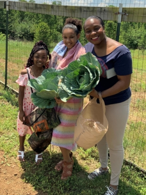 An adult and two children smile while holding lettuce.