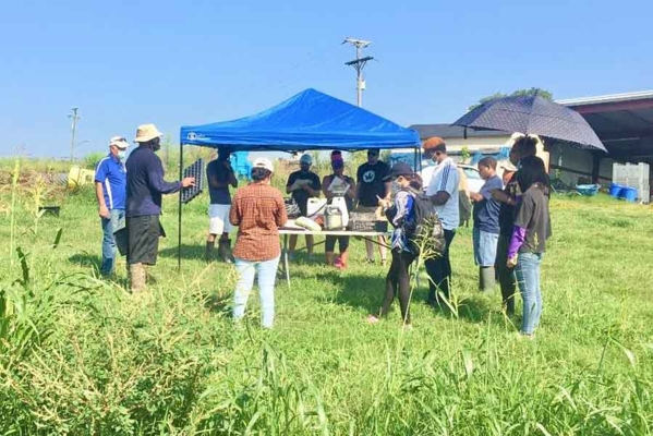 Group gathered under a tent in a field.