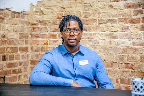 Man sitting at table with brick wall behind him.