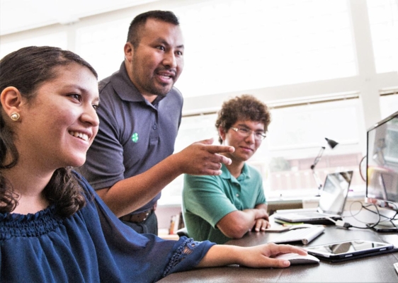 4-H instructor helps two students sitting in front of computers.