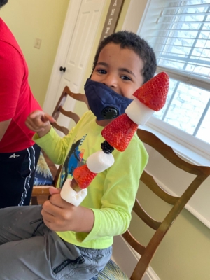 Child holds up a fruit kabob.