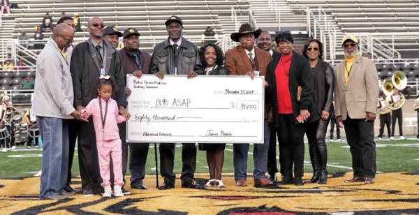 Group holds large check on football field.