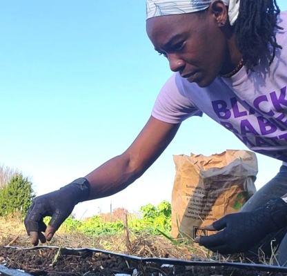 Izula Maximillen on her knees in the soil planting seeds.