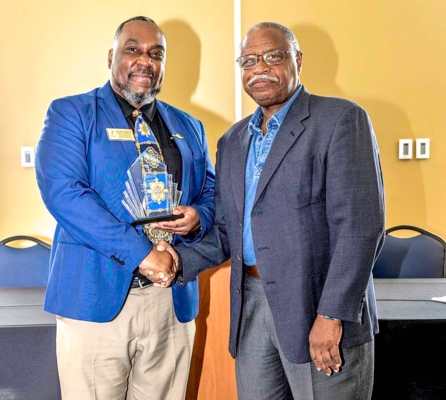 Woodie Hughes Jr. holds award while shaking hands with Dr. Mark Latimore Jr."