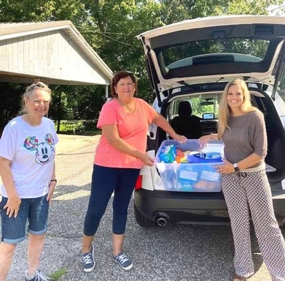 Three women loading items into trunk of vehicle.