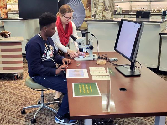 A student looks into a microscope as he learns from a facilitator.